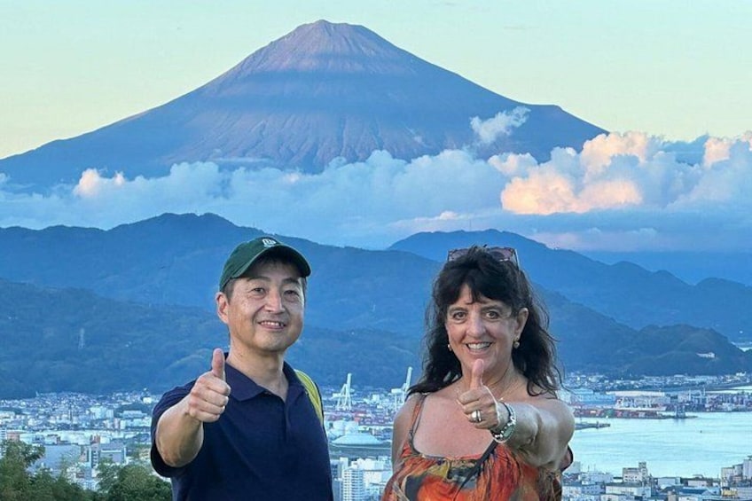 Two people giving thumbs up in front of a volcano with a cityscape in the background. 3