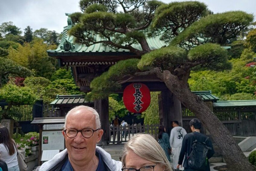 A traditional Japanese gate with a red sign, surrounded by lush greenery and a pagoda in the background. 2