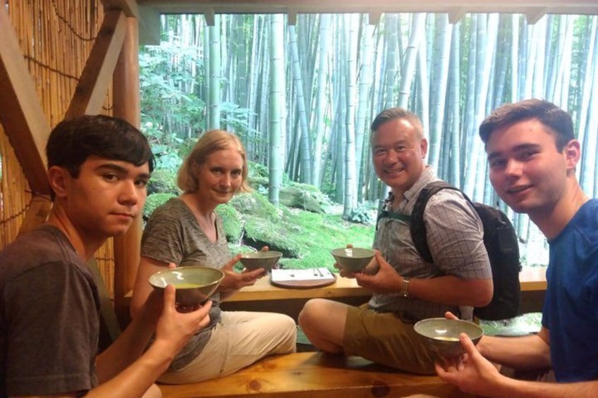 Four people sitting at a table with bowls, in a room with bamboo outside. 3