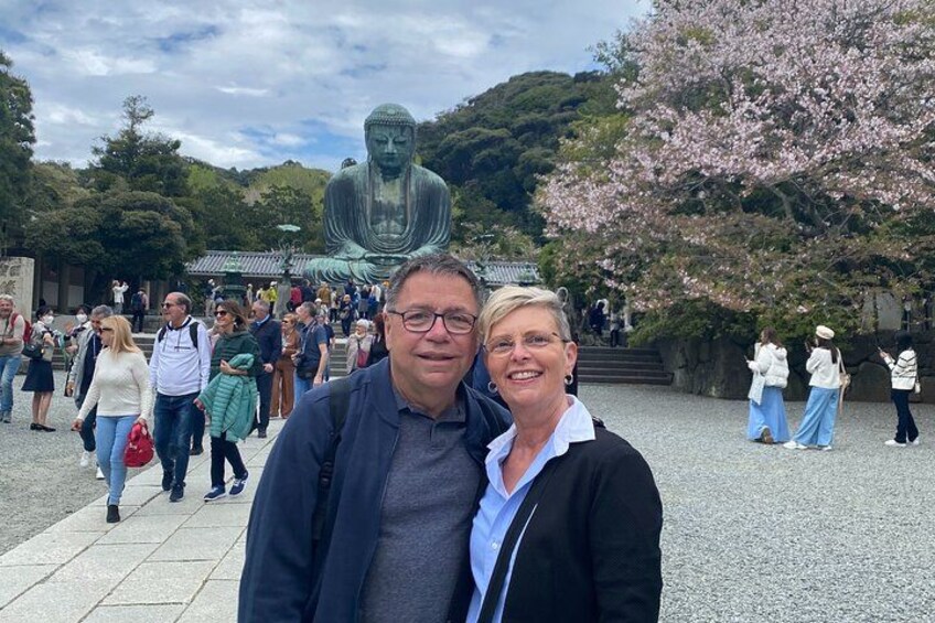 A large Buddha statue, people walking, and cherry blossoms. 5