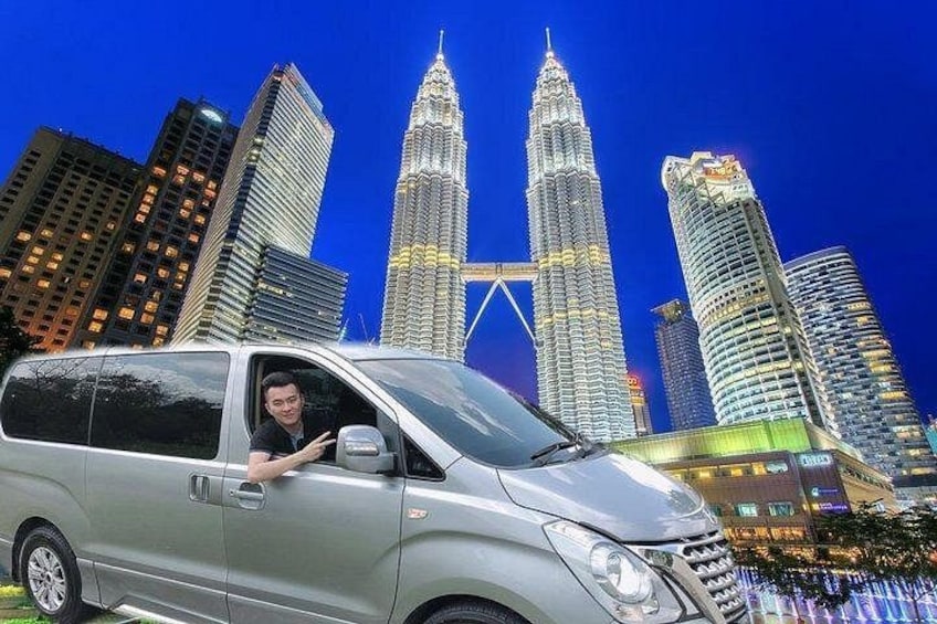 Een zilveren busje geparkeerd voor de Petronas Twin Towers, met iemand daarin. 1
