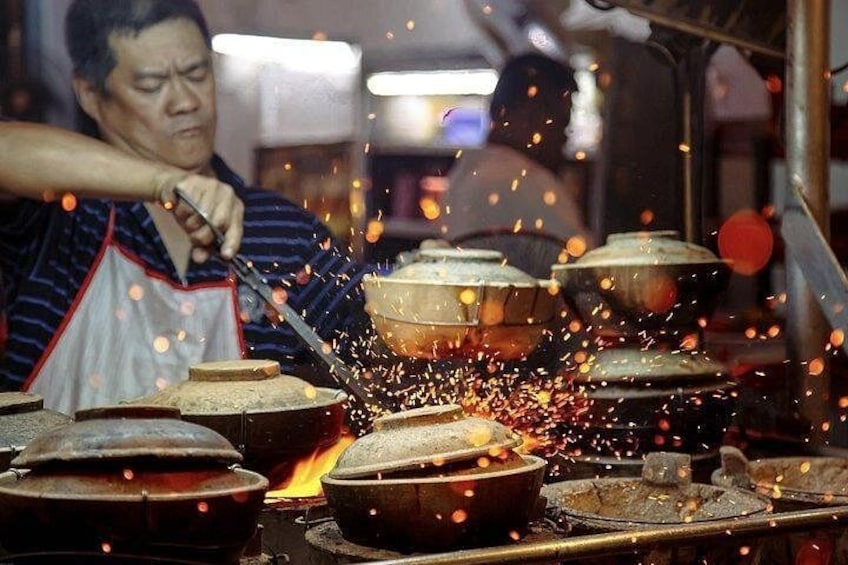 Iemand gebruikt een brander om eten in een pan te bereiden, met zichtbare vlammen en vonken. 3