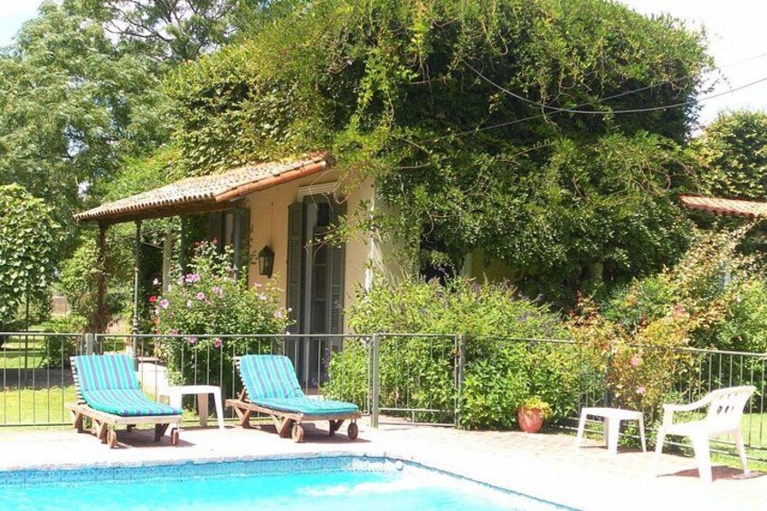 A swimming pool with lounge chairs, a small house with a tiled roof, and lush greenery. 3