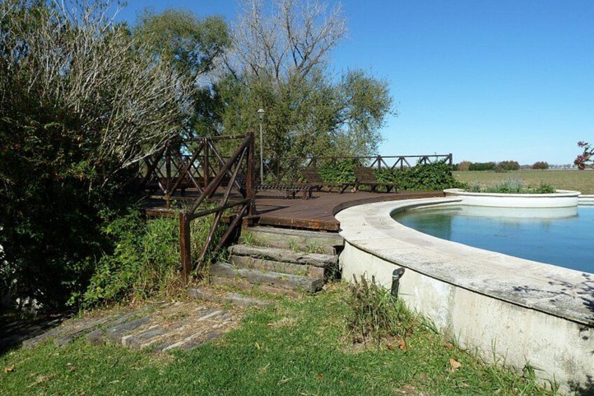 A wooden bridge, a swimming pool, and a grassy area with trees. 4