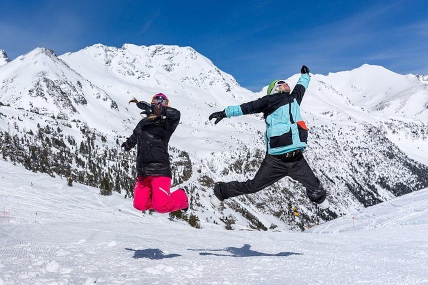 Two people jumping on a snowy mountain with a clear blue sky. 2