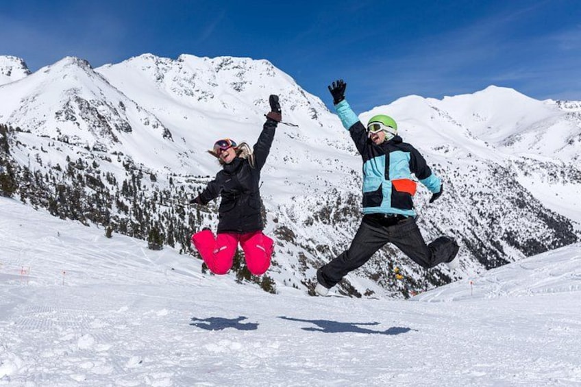 Two people jumping on a snowy mountain with snow-covered peaks in the background. 1