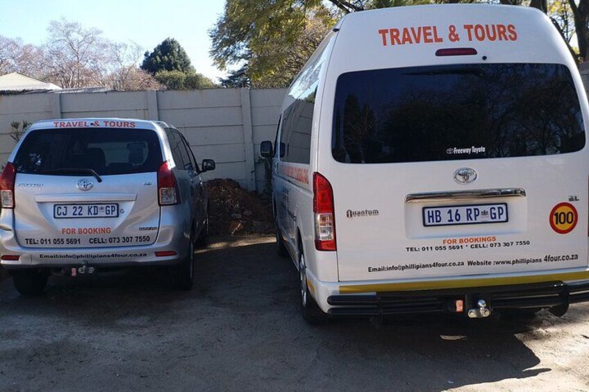Two white vans with 'TRAVEL & TOURS' text on the back, parked on a dirt road. 2