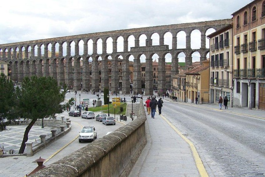 A historic aqueduct with arches, a paved street, and buildings. 1