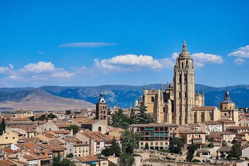 A cathedral with a tall bell tower, surrounded by historic buildings and mountains in the background. 5