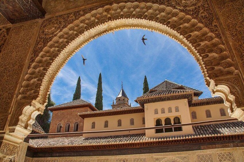 Un arco decorativo enmarca un edificio con tejado de azulejos y dos torres. 1