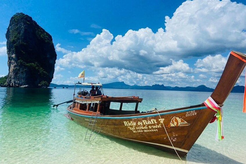 A wooden boat with a flag, a clear blue sky, and a large rock formation in the background. 2