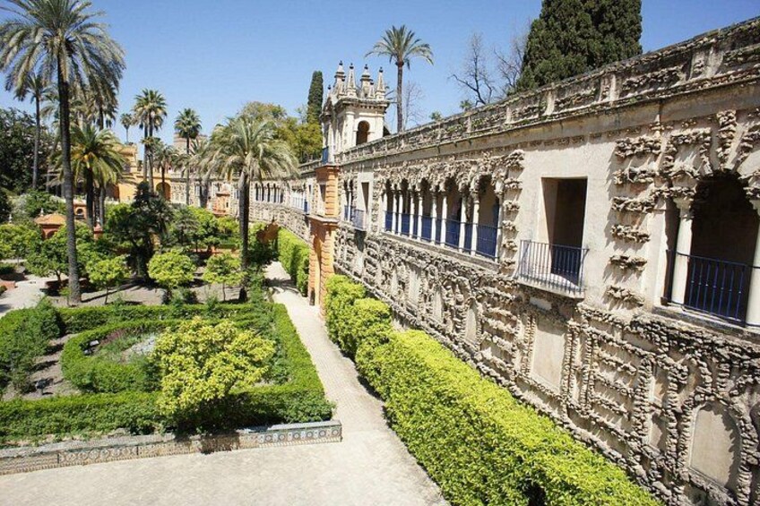 A historic building with ornate architecture, a garden with various plants, and palm trees in the background. 1