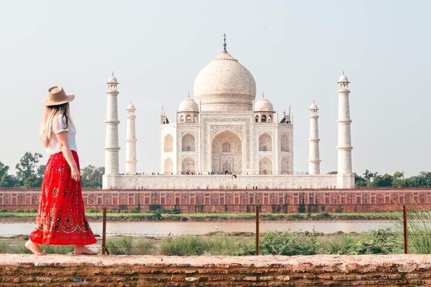 A woman in a red dress and hat walking by the Taj Mahal. 1