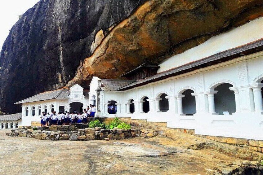 A white building with arched windows and a large rock formation in the background. 1