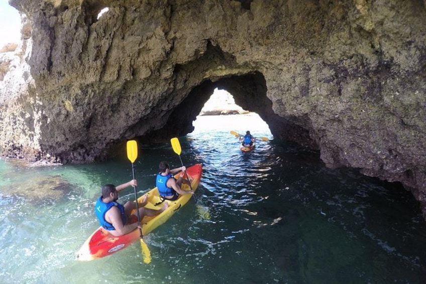 People kayaking through a rocky cave opening. 3