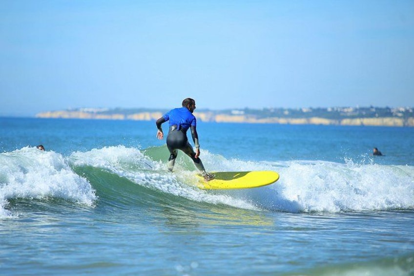 En surfer i en blå våddragt rider på en gul surfbræt på en bølge. 1
