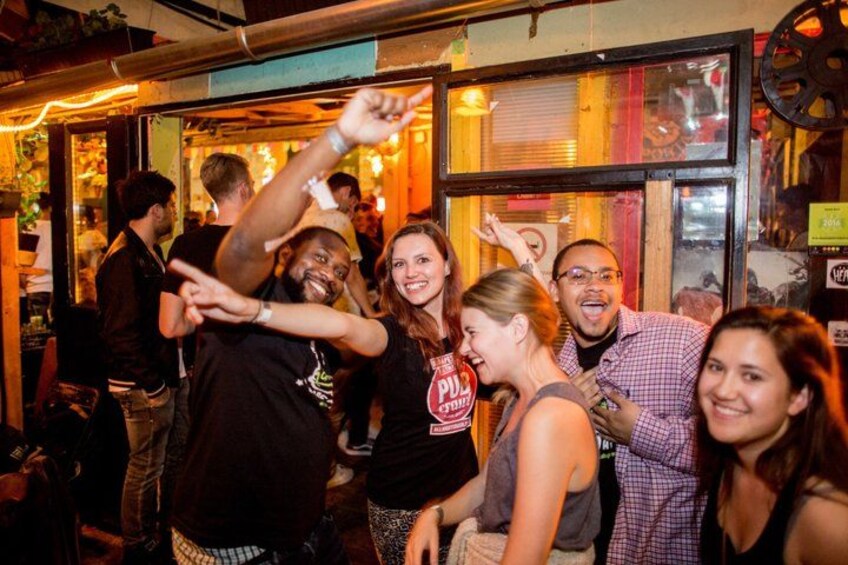 A group of people gathered in a lively indoor setting with a bar or restaurant in the background. 4