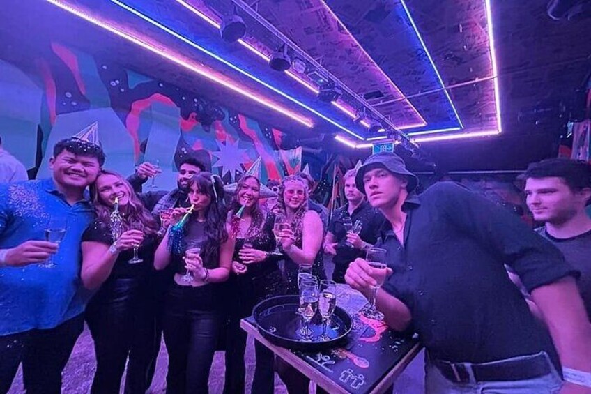 A group of people at a party with a DJ booth and neon lights. 3
