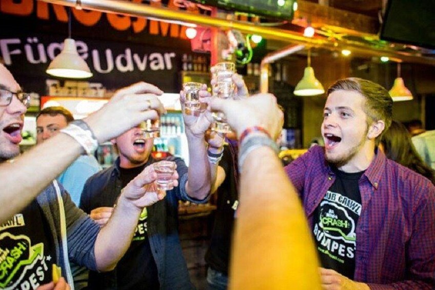 People toasting with drinks in a bar with a sign that reads 'Füchse Udvar.' 5