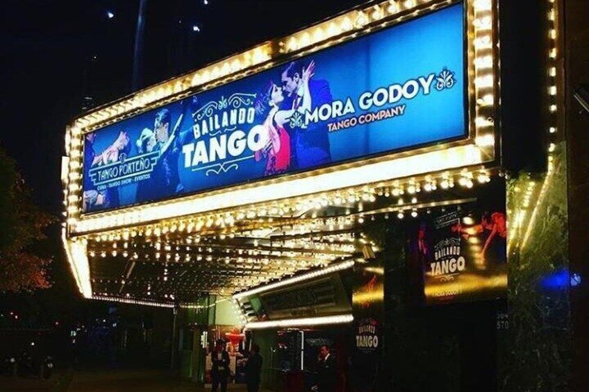 Un théâtre en plein air, illuminé de mille feux, avec une enseigne annonçant les spectacles « Balando Tango » et « Mora Godoy Tango Company ». 3