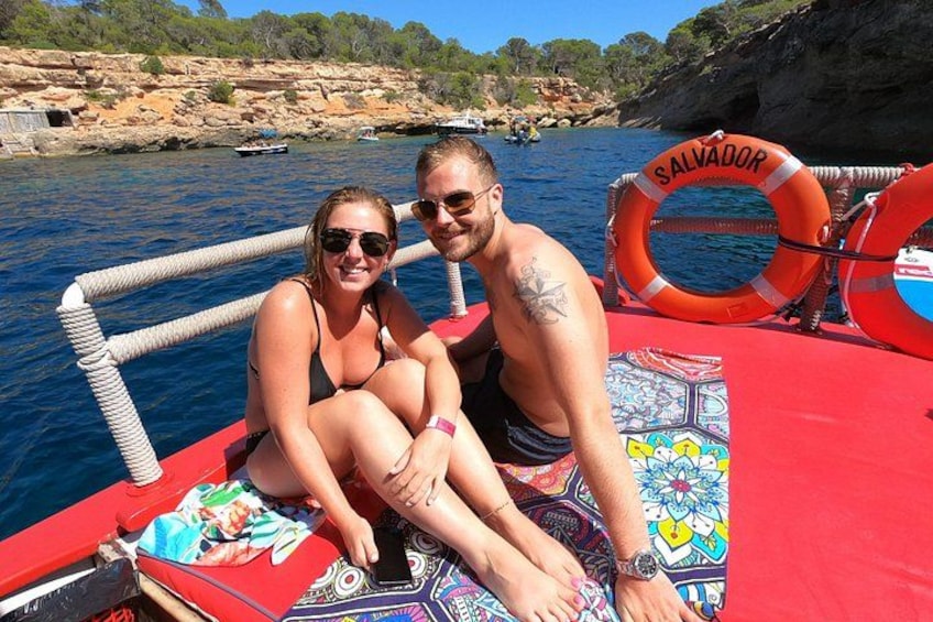 Två personer i en båt, med en livboj märkt med texten ”SALVADOR” och en färgglad matta. 2