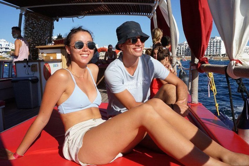 A person sitting on a red deck on a boat, with a cityscape in the background. 2