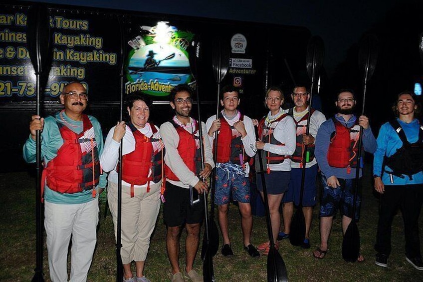 A group of people holding paddles, standing in front of a sign that reads 'Florida Adventures Kayaking.' 2