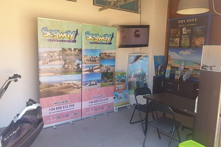 A room with a desk, chairs, a television, and promotional posters for a travel company. 2