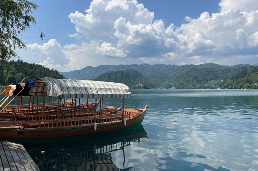 Un bateau en bois avec un pont couvert, sur un lac paisible, entouré de montagnes et sous un ciel dégagé. 1