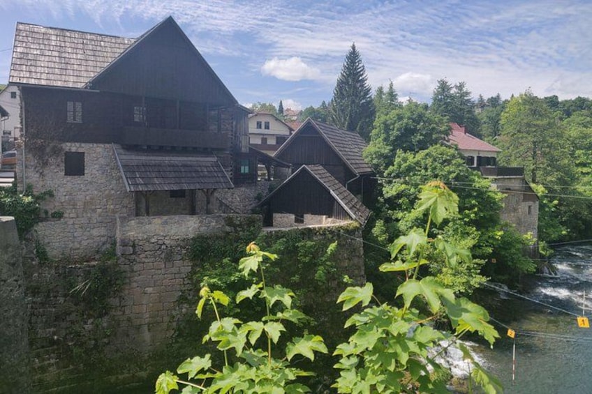 A historic stone building with a steep roof, surrounded by lush greenery and a river. 3
