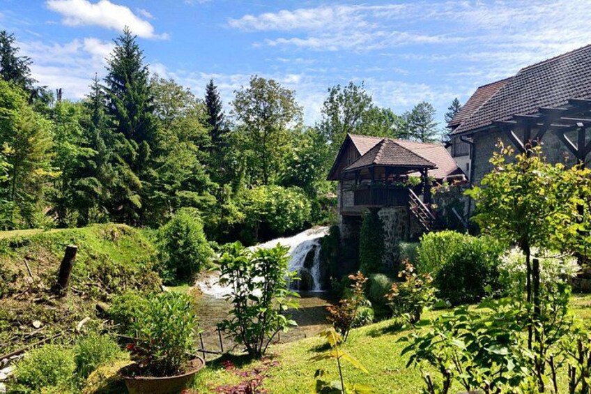 A lush garden with a waterfall, a wooden structure, and a stone building. 3
