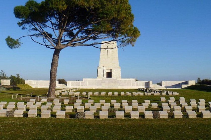 A memorial with a tall monument, a large tree, and a cemetery with headstones. 1