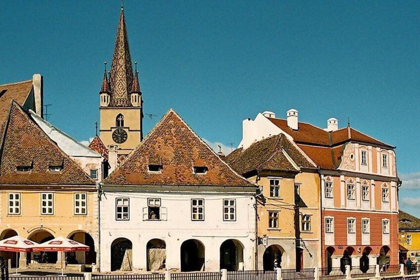 A historic town square with traditional buildings, a church tower, and a clear blue sky. 1