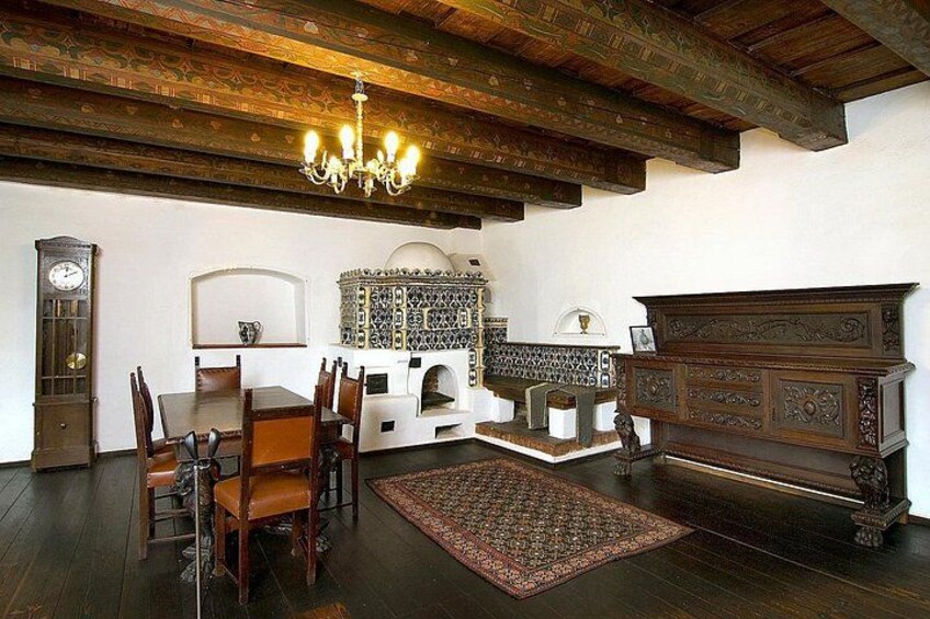 A room with wooden beams, a chandelier, a clock, a patterned cabinet, a fireplace, and a wooden cabinet. 3