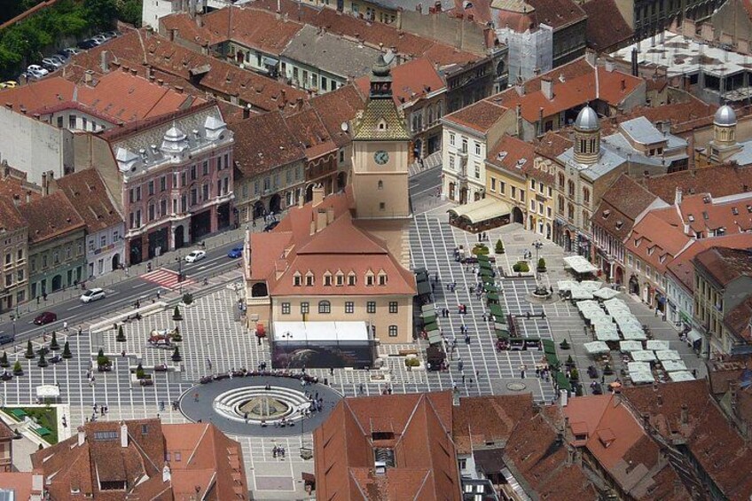 A historic square with a central building, a clock tower, and surrounding red-roofed structures. 2