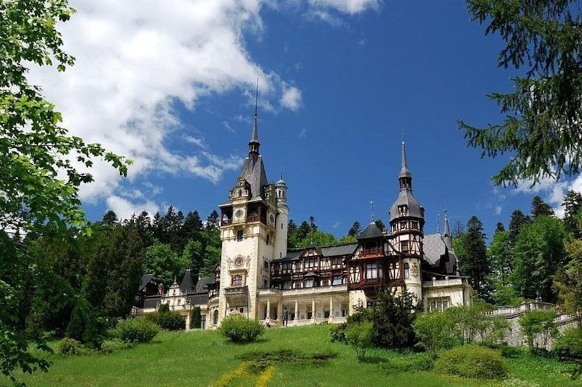 A large, historic building with two prominent towers, surrounded by lush greenery and a clear blue sky. 2
