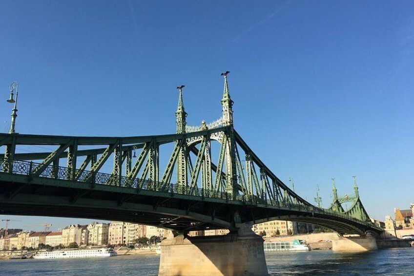 A green steel bridge with ornate towers, spanning over a river with buildings in the background. 4