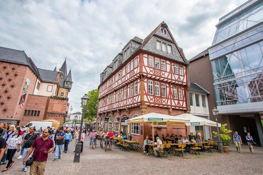 A cobblestone street with traditional half-timbered buildings, outdoor seating at a café, and pedestrians. 5