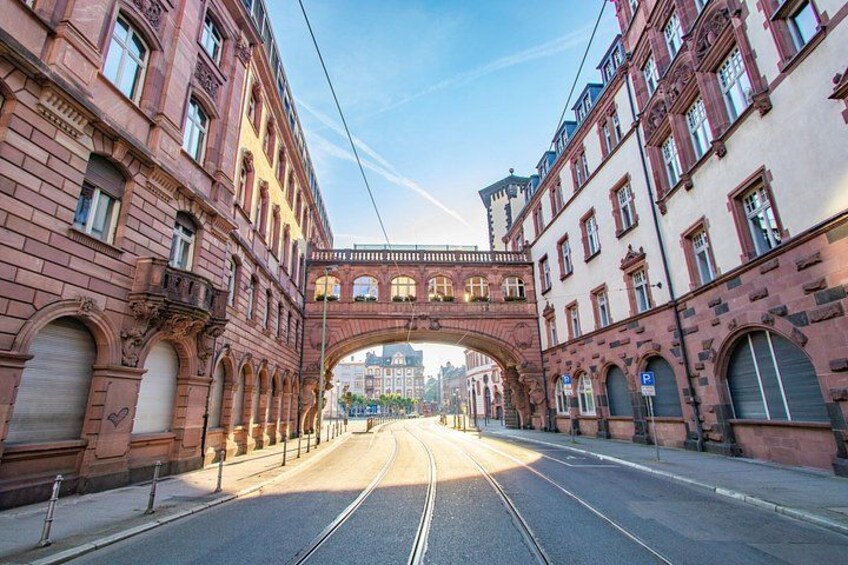 A street with a red brick archway, tram tracks, and buildings with arched windows. 2