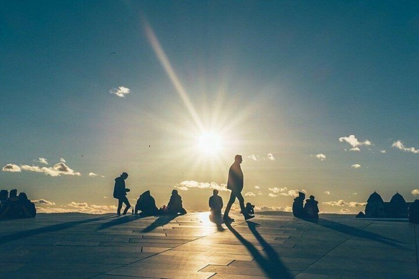 A sunset with people walking and sitting on a paved area. 3
