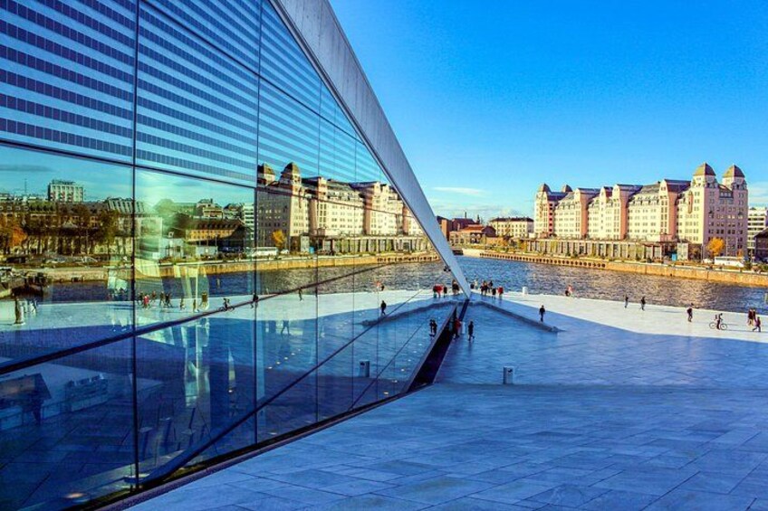 A modern glass building with a unique angular design, a waterfront promenade, and historic buildings in the background. 5