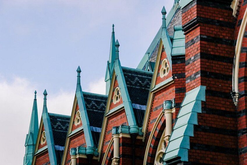 A building with red brick walls and green roof tiles, featuring pointed, ornate roof structures. 1