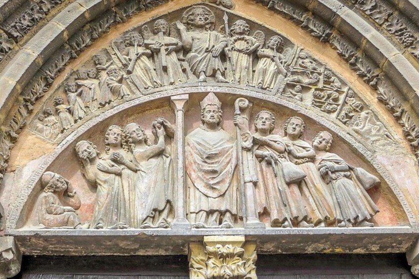 A detailed stone carving of a religious scene with figures, a central figure holding a staff, and a halo. 4