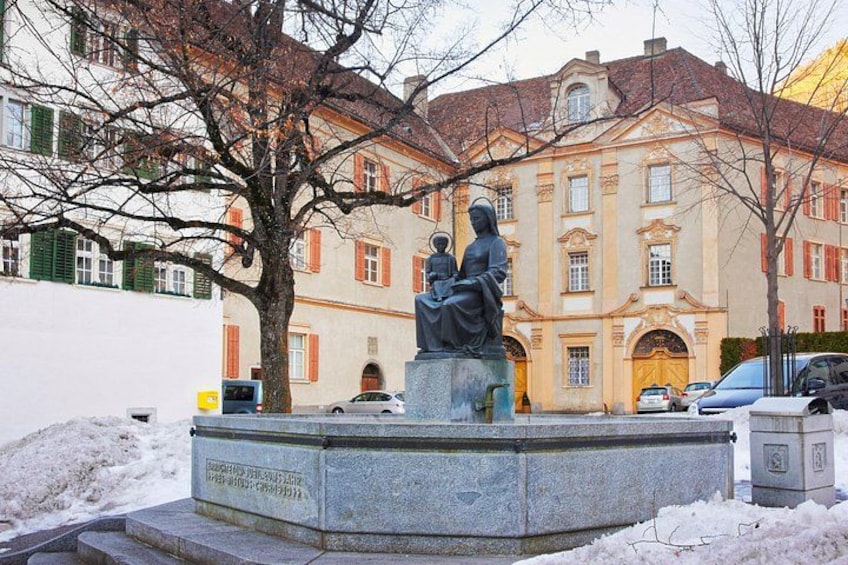 A statue of two figures on a pedestal in a public square with a building in the background. 1