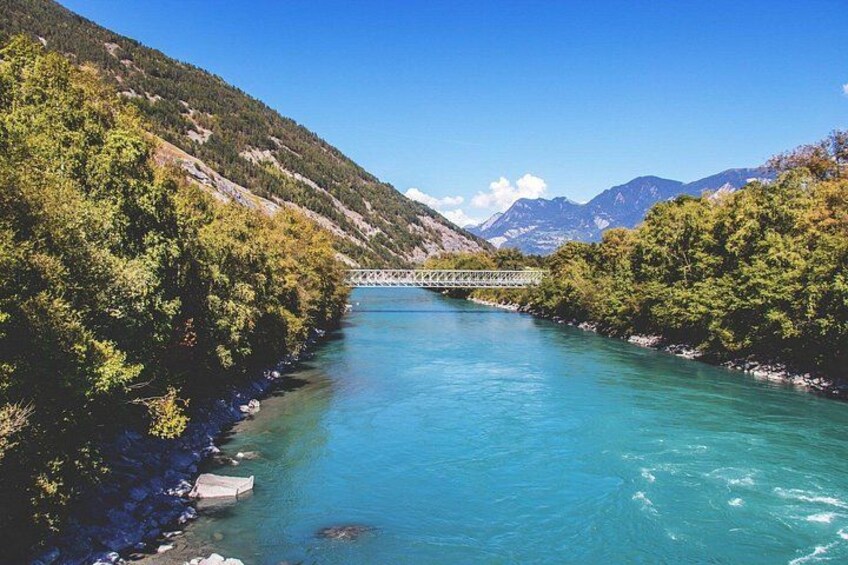 A river with a bridge, surrounded by green hills and mountains. 2