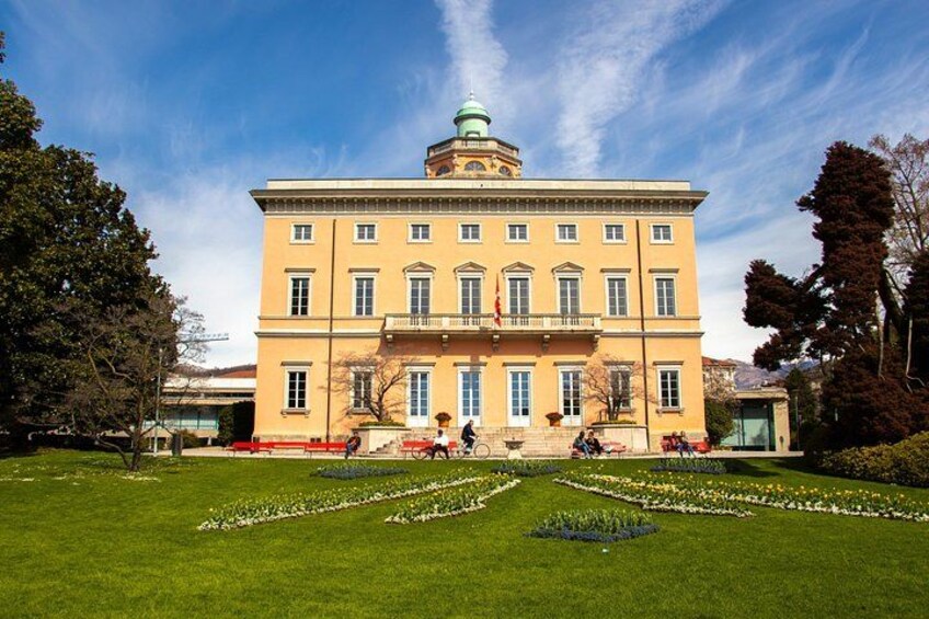 Un grande edificio giallo con una cupola verde, circondato da un prato curato e aiuole fiorite. 2