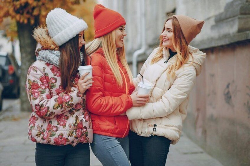 Tres personas con abrigos de invierno, una sosteniendo una taza de café, de pie en una calle de la ciudad. 3