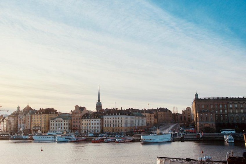 A waterfront cityscape with historic buildings, a prominent church spire, and several boats docked along the river. 3