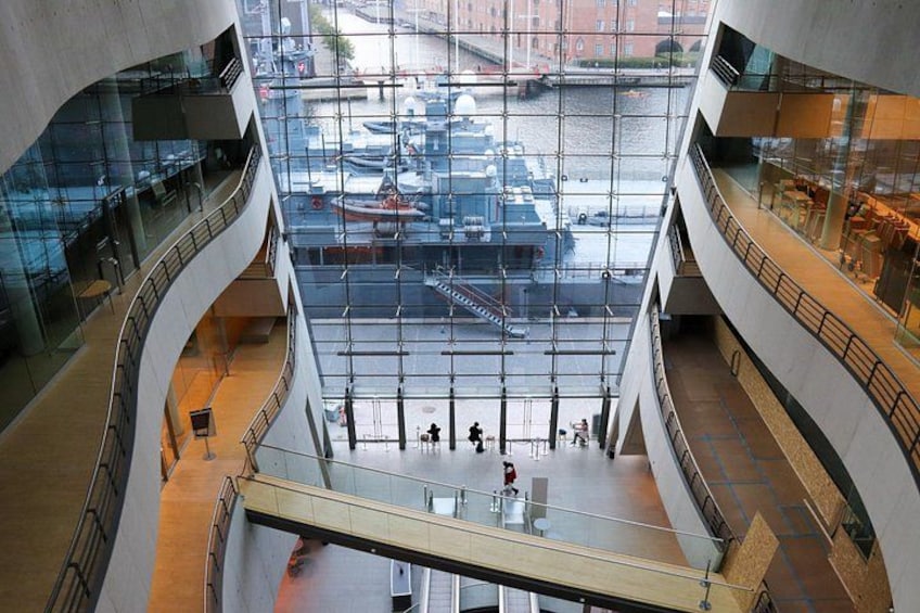 A modern building with multiple floors, large glass windows, and a view of a busy street with boats. 3