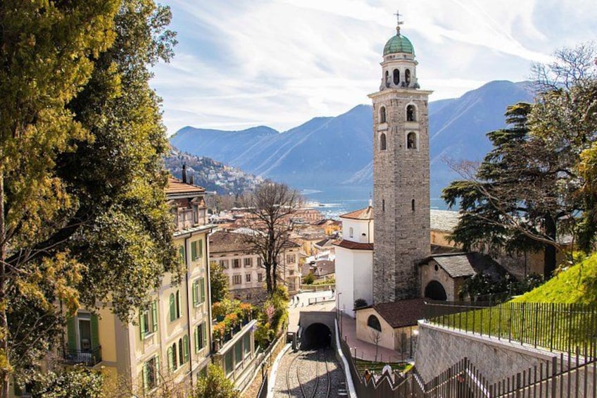 A mountain town with a prominent tower, lush greenery, and a clear view of the valley below. 1